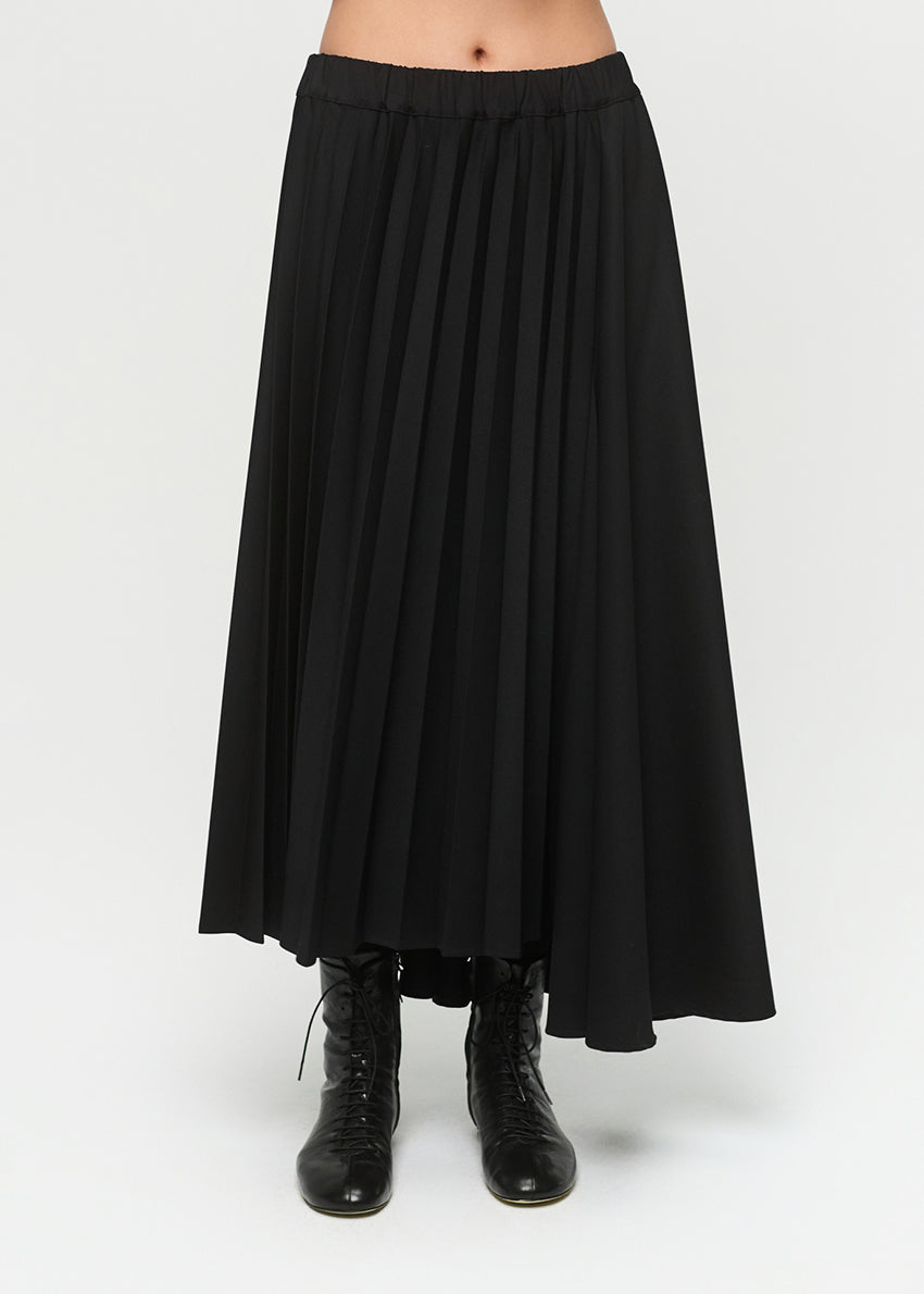 Woman wearing a light gray top and pleated skirt on a white background