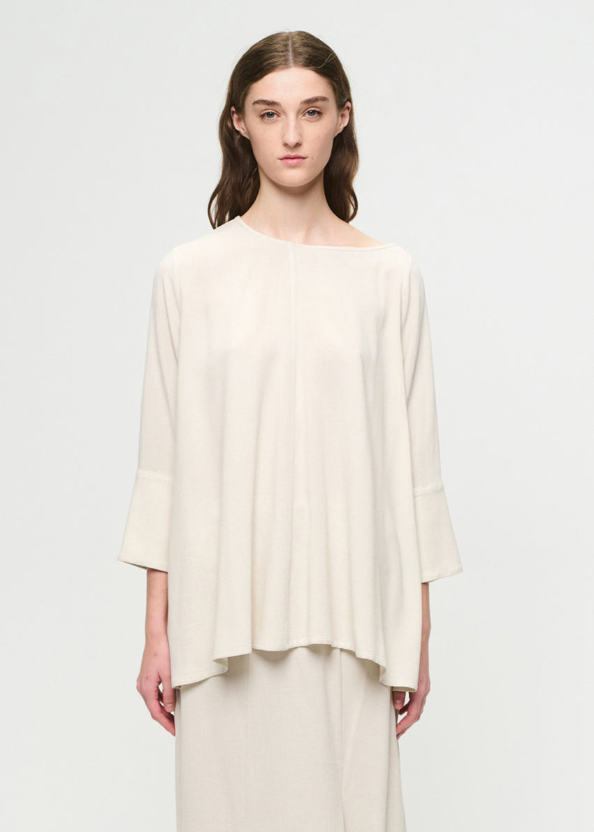 Woman wearing a cream-colored top and pants on a light gray background