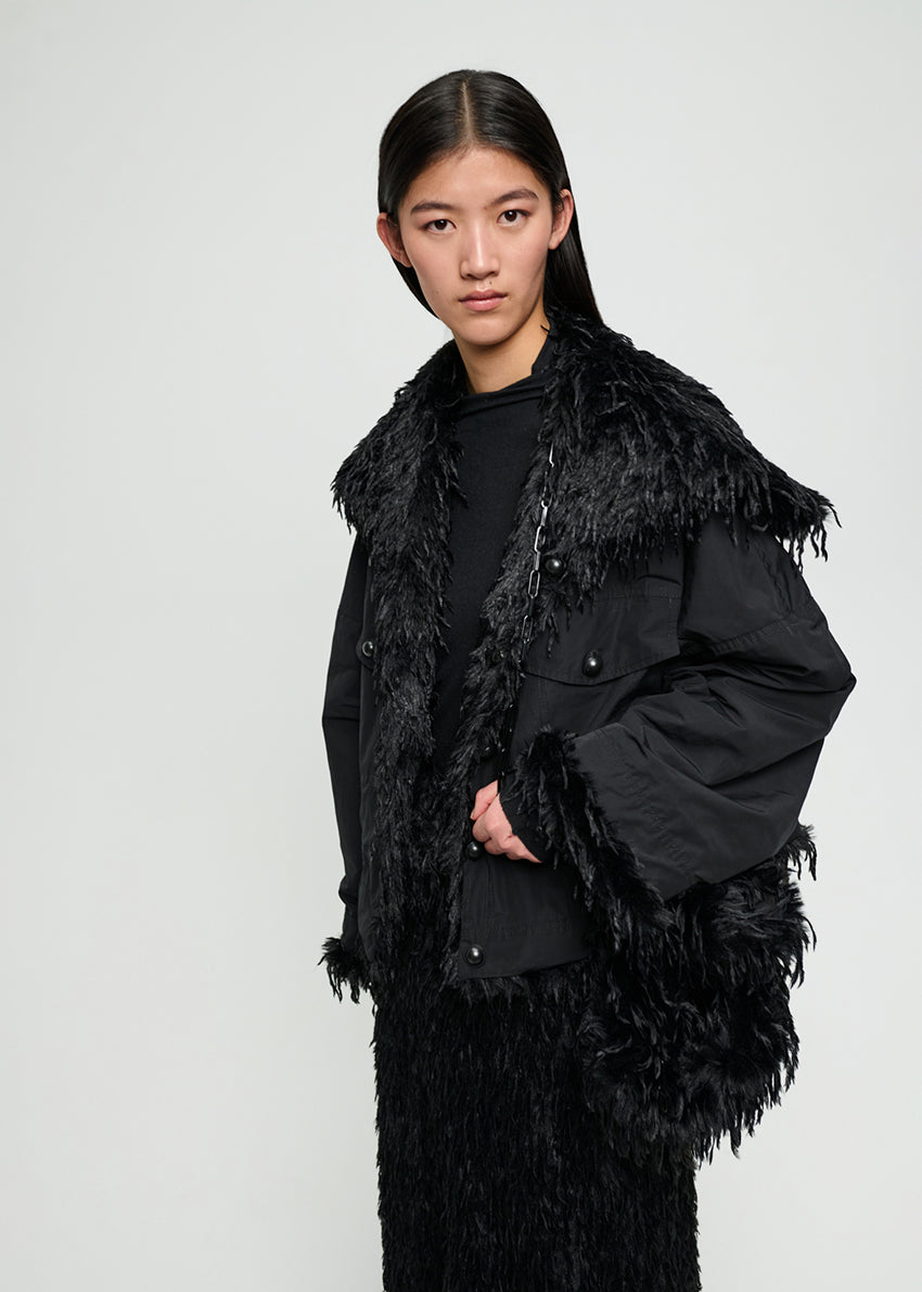 Person wearing a black fur-trimmed coat against a plain background