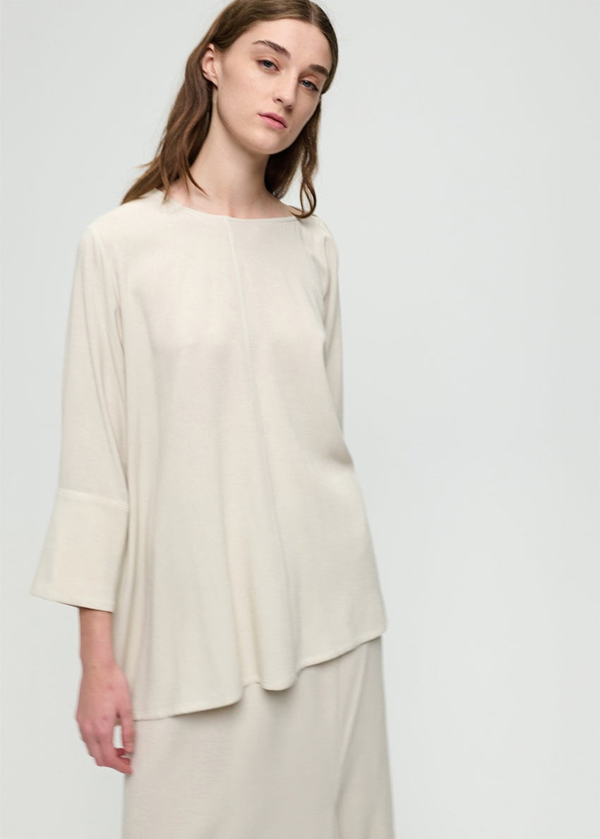 Woman wearing a cream-colored top and pants on a light gray background