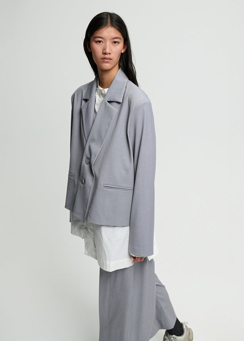 Person wearing a gray blazer over a white outfit on a plain background