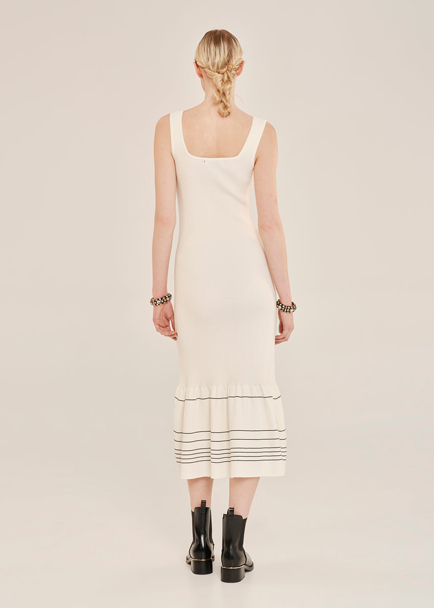 Woman wearing a white sleeveless dress with black trim on a plain background