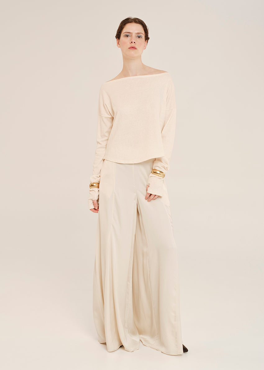 Woman wearing a beige off-shoulder top and wide-leg pants with gold accents on a white background