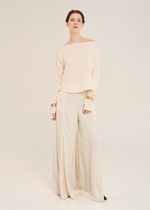 Woman wearing a beige off-shoulder top and wide-leg pants with gold accents on a white background