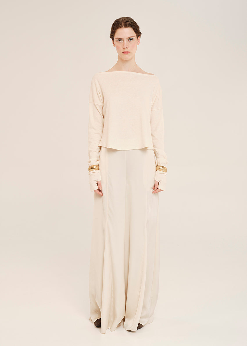Woman wearing a beige off-shoulder top and wide-leg pants with gold accents on a white background
