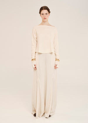 Woman wearing a cream-colored outfit with long sleeves and wide-leg pants on a plain background