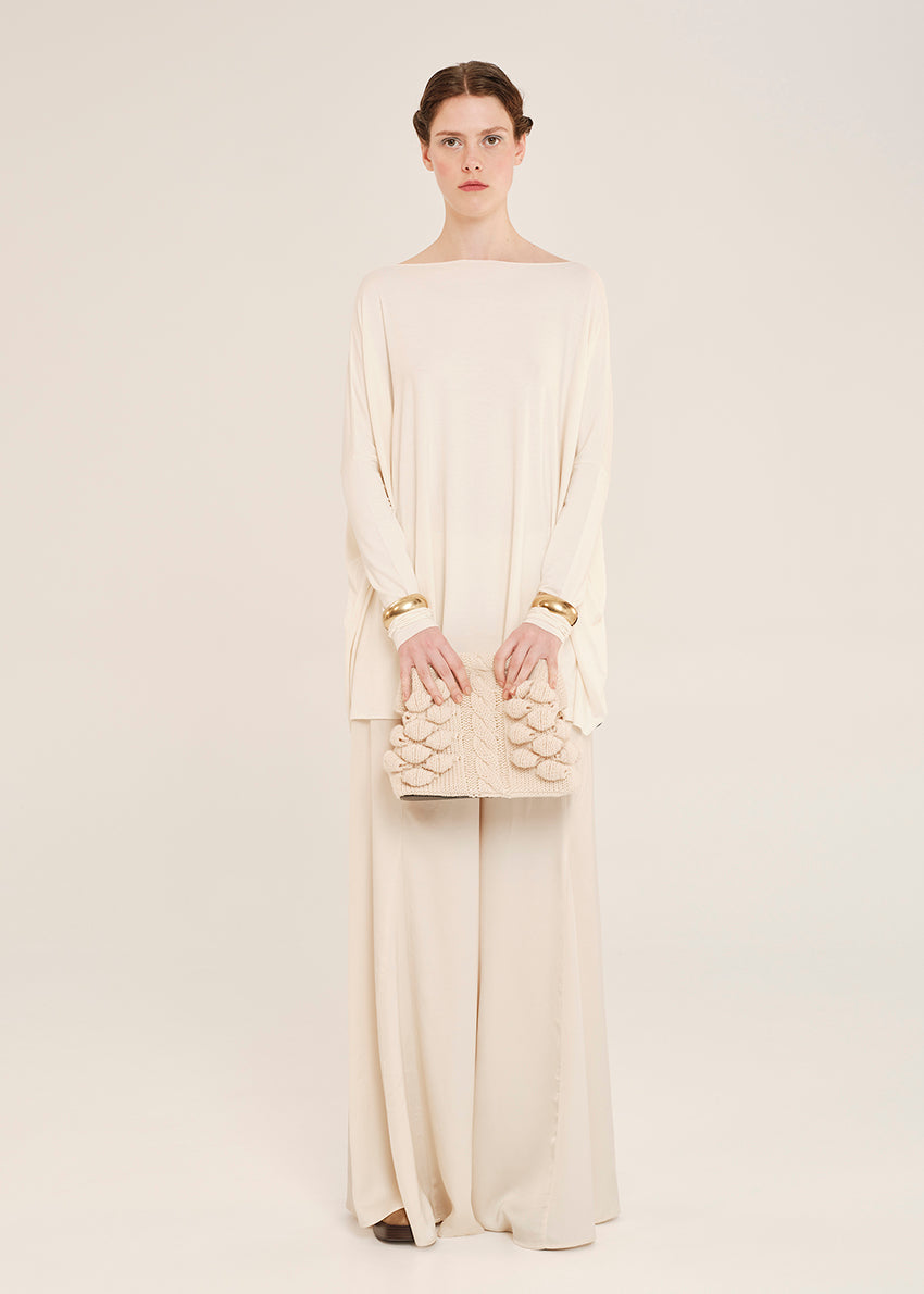 Woman wearing a cream-colored oversized top with a matching handbag on a plain background