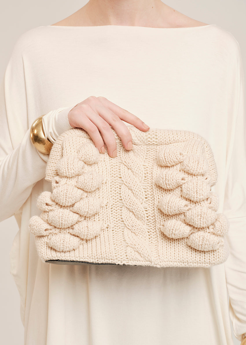 Cream-colored knitted clutch held by a person wearing a white sweater.