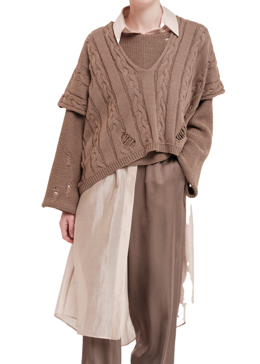 Person wearing a brown cable knit vest over a white shirt with beige pants on a white background