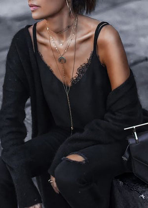 A woman wearing a black lace top with adjustable straps and delicate lace trim, paired with high-waisted jeans and accessorized with multiple necklaces.
