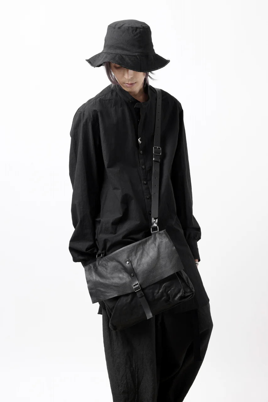 Person wearing a black outfit with a black bucket hat and carrying a black bag on a white background