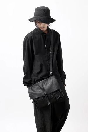 Person wearing a black outfit with a black bucket hat and carrying a black bag on a white background