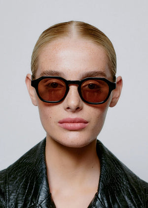 Person wearing sunglasses and a black leather jacket against a plain background