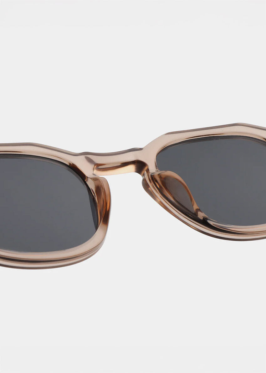 Sunglasses with a champagne frame and dark lenses on a light gray background