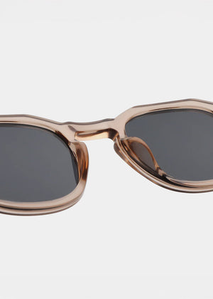 Sunglasses with a champagne frame and dark lenses on a light gray background