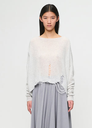 Woman wearing a light gray sweater with lace details and a gray pleated skirt on a white background