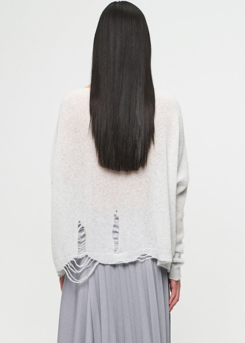 Person wearing a light gray sweater with lace details on a white background