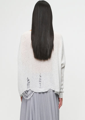 Person wearing a light gray sweater with lace details on a white background