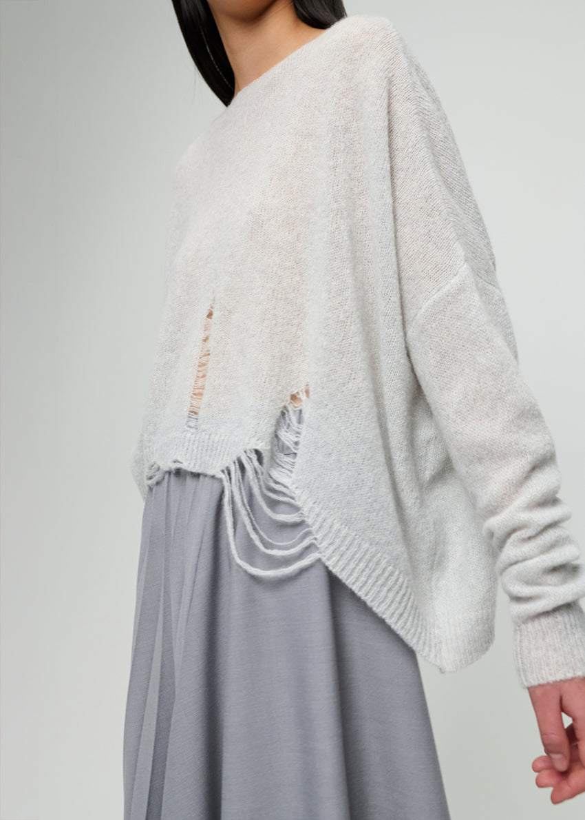 Person wearing a light grey sweater and grey skirt on a plain background