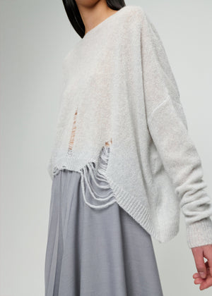 Person wearing a light grey sweater and grey skirt on a plain background