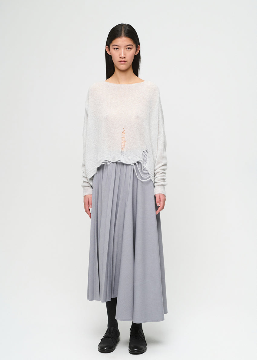 Woman wearing a light-colored top and gray pleated skirt on a white background