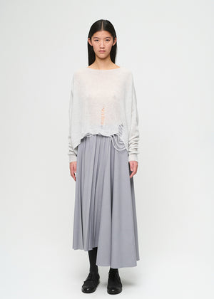 Woman wearing a light-colored top and gray pleated skirt on a white background