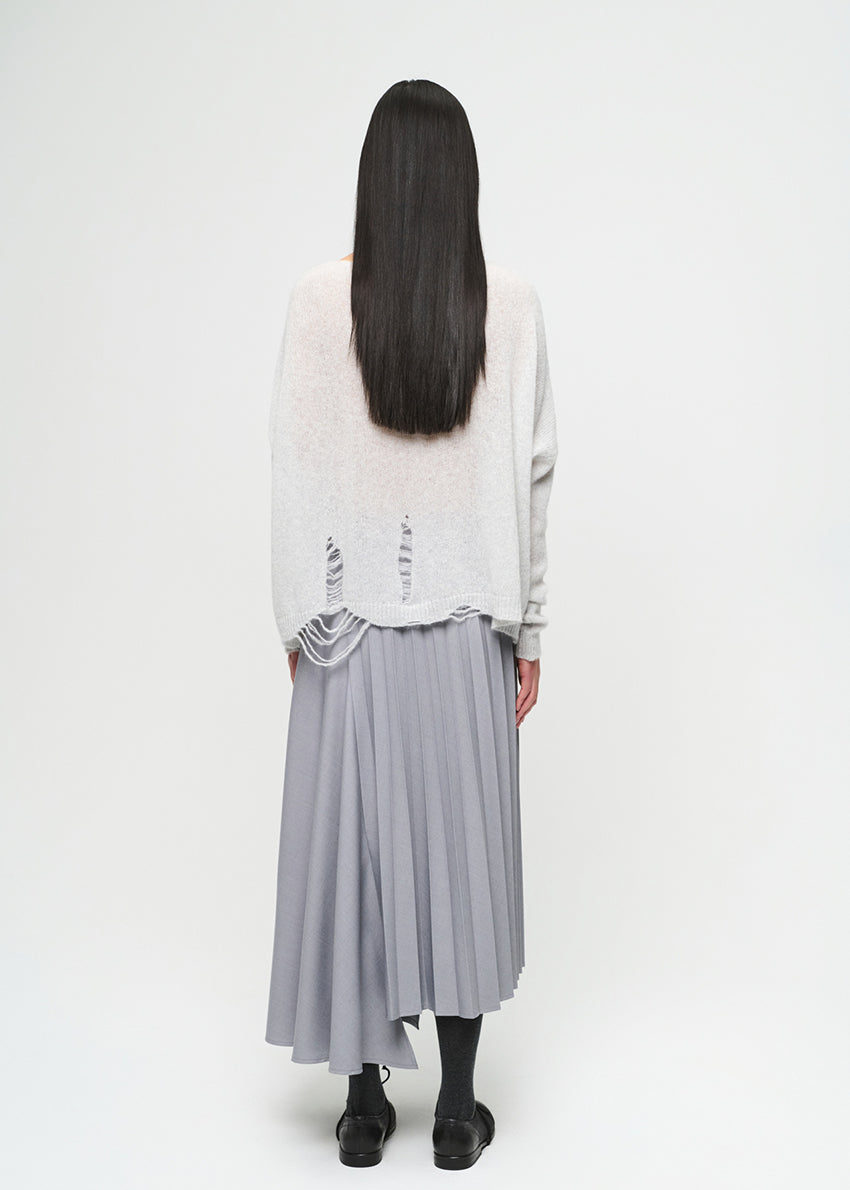 Person wearing a light-colored top and gray pleated skirt on a white background