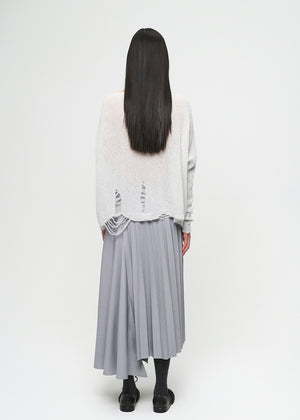 Person wearing a light-colored top and gray pleated skirt on a white background