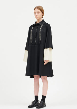 A model wearing a black midi dress with 3/4 sleeves and a shirt neckline with a button closure. The dress has a loose fit and a deep V-neckline.