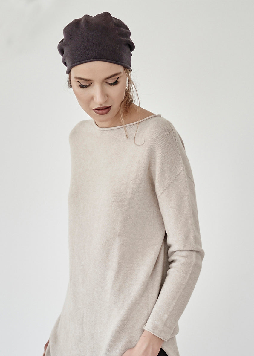 Woman wearing a beige sweater and dark headscarf on a plain background