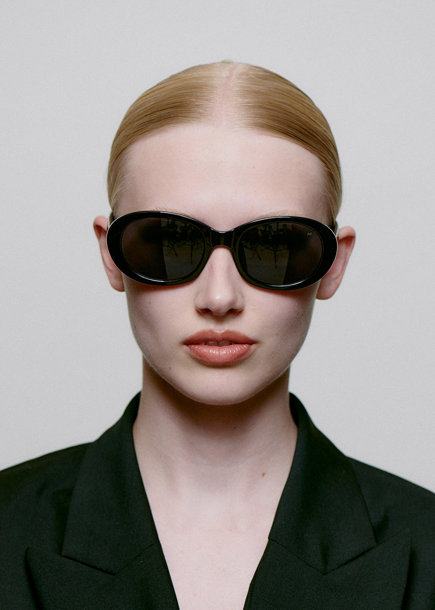 Person wearing black sunglasses and a black outfit against a plain background