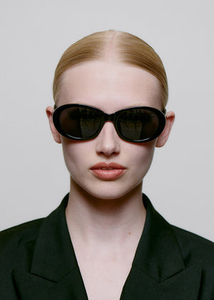 Person wearing black sunglasses and a black outfit against a plain background