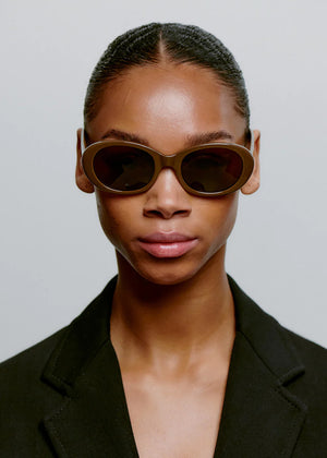 Woman wearing brown sunglasses and a black blazer against a plain background