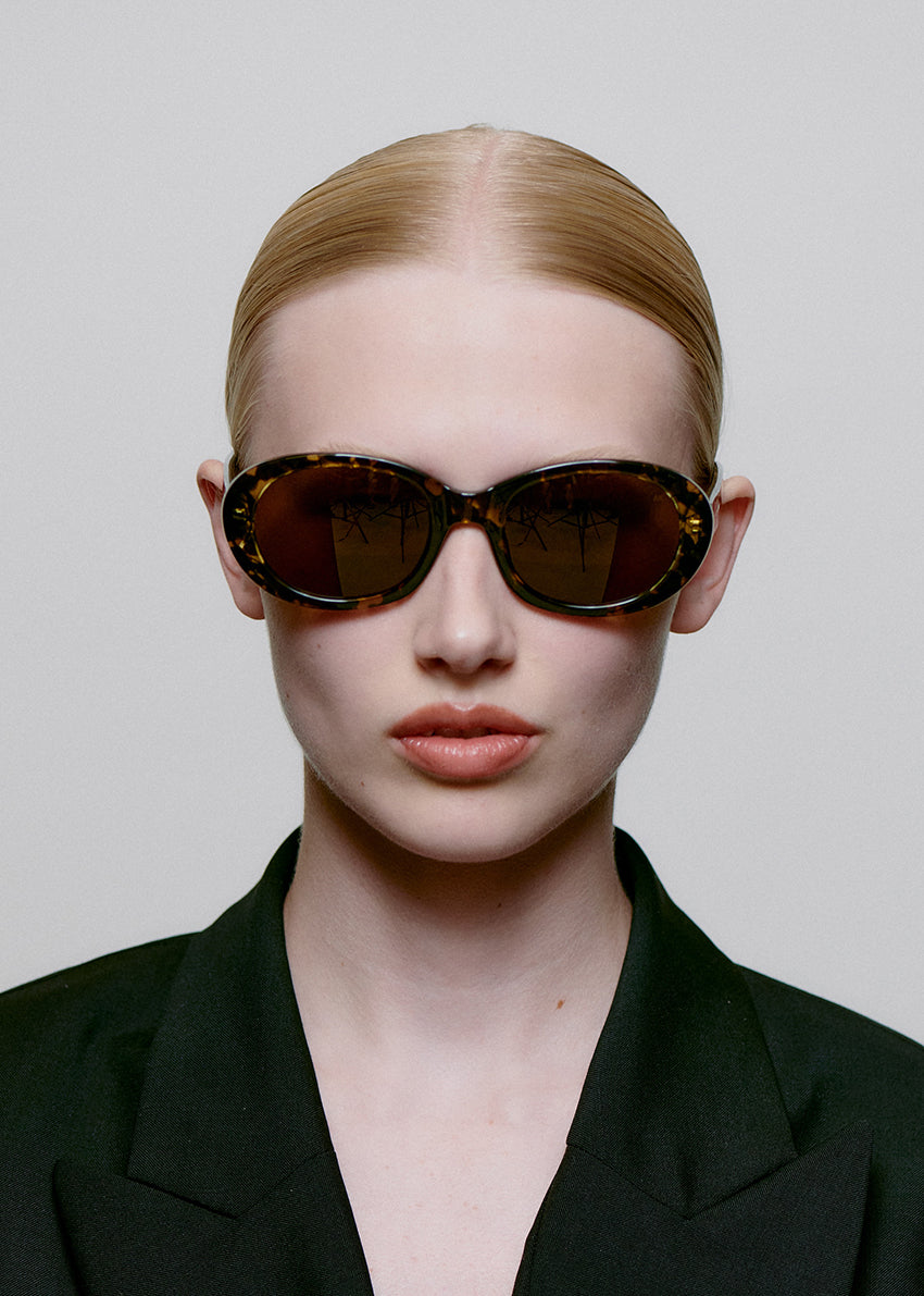 Person wearing a black outfit and sunglasses against a plain background