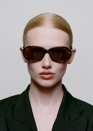 Person wearing a black outfit and sunglasses against a plain background