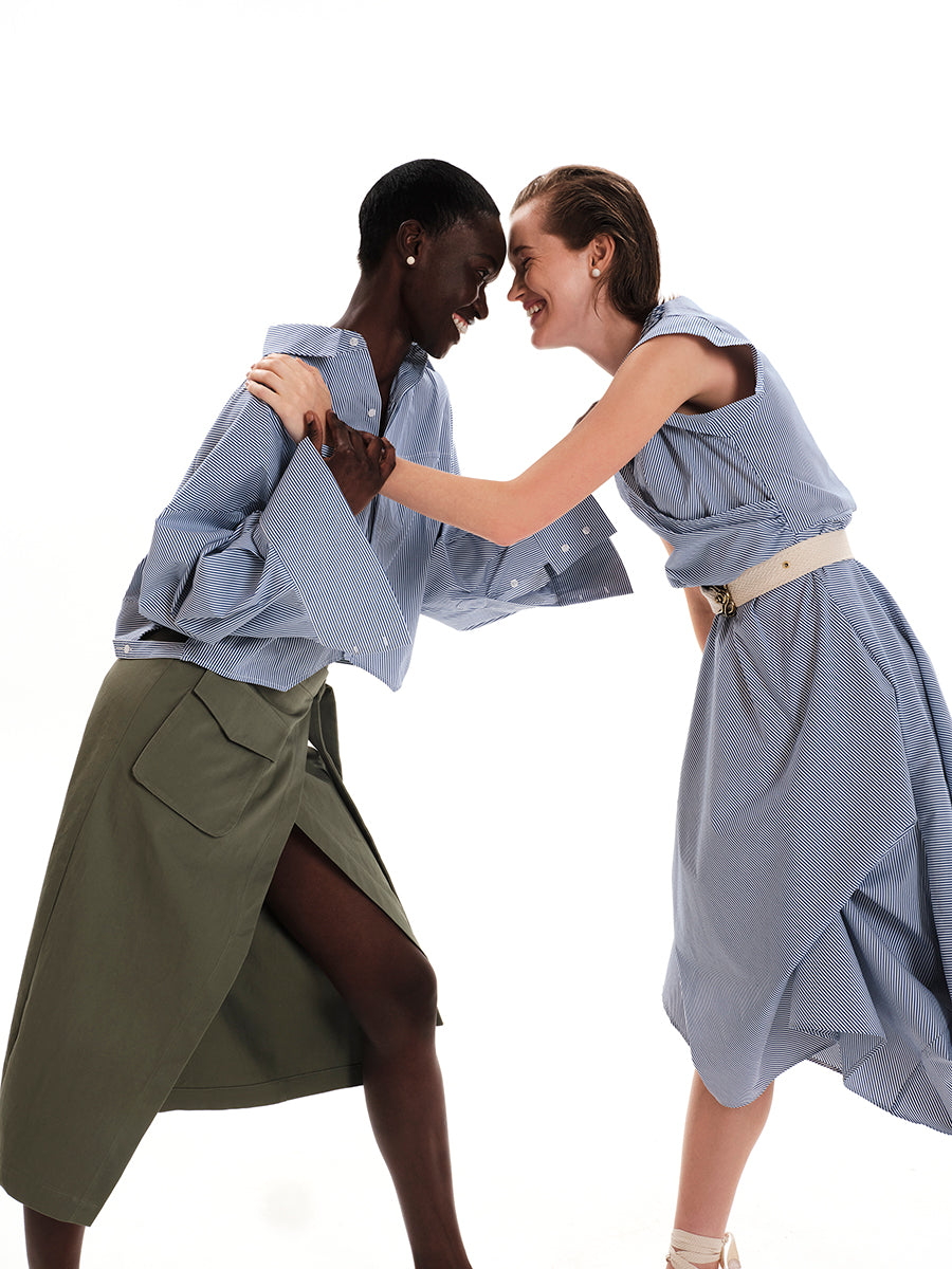 A model wearing a green wrap-style skirt with a large pocket and a front slit, paired with a blue shirt.