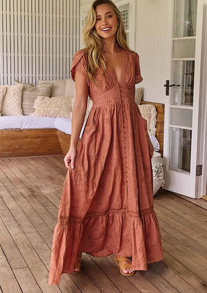 A woman standing on a porch wearing a brown, solid pattern, Maxi dress with short flutter sleeves, V-neckline, and ruffled hem.
