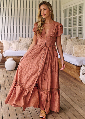 A woman standing on a porch wearing a brown, solid pattern, Maxi dress with short flutter sleeves, V-neckline, and ruffled hem.