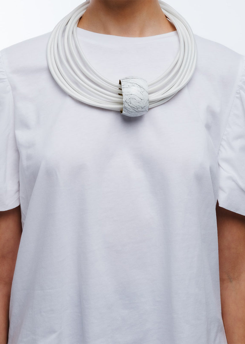 A white, multi-layered choker necklace with a cylindrical pendant and dimgray details, designed by Katerina Vassou.