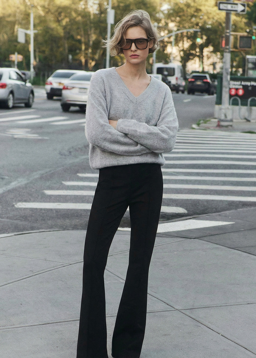 Woman in a gray sweater and black pants standing on a city street.