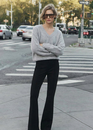 Woman in a gray sweater and black pants standing on a city street.