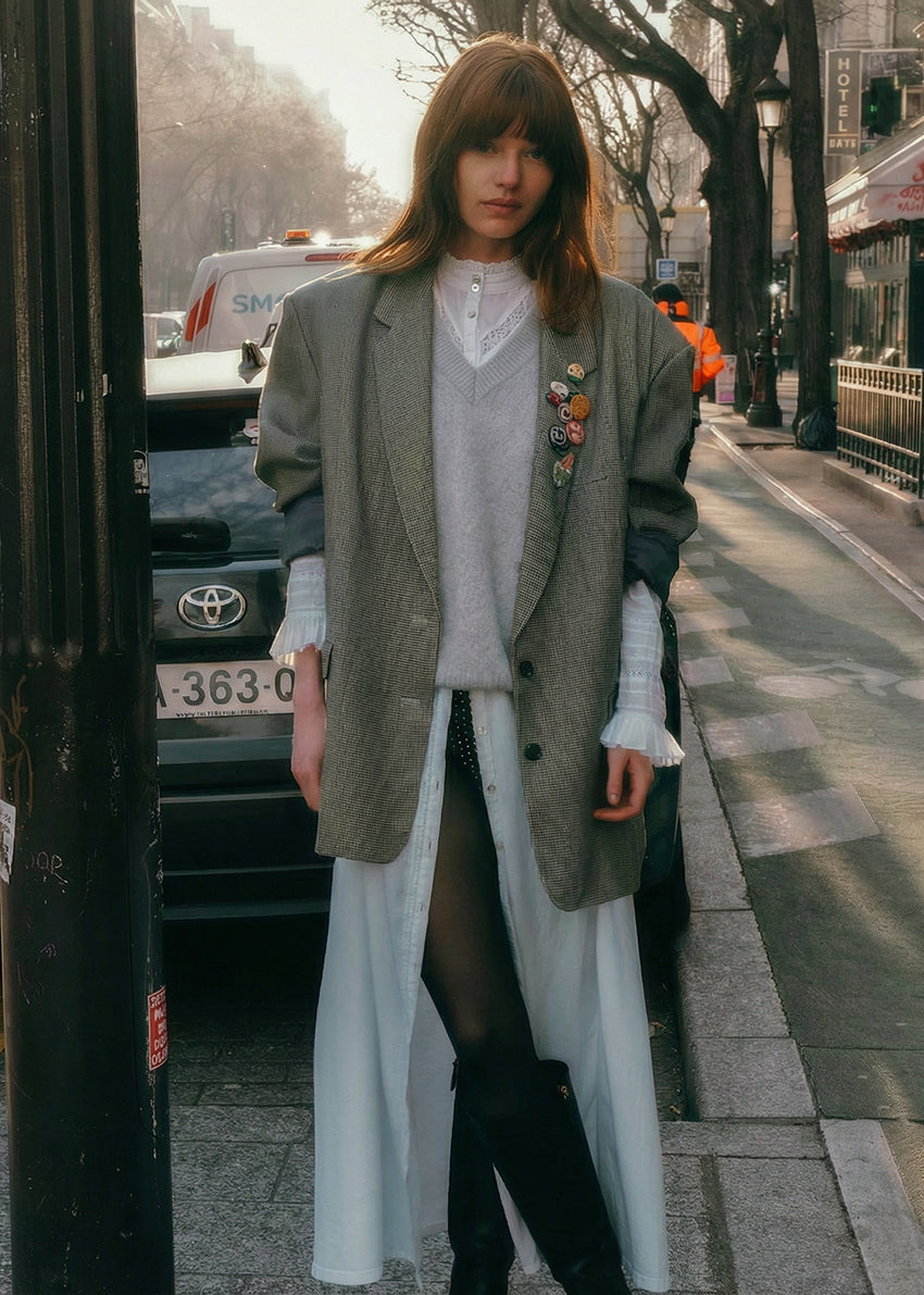 Woman walking on a city street wearing a long coat and white pants.