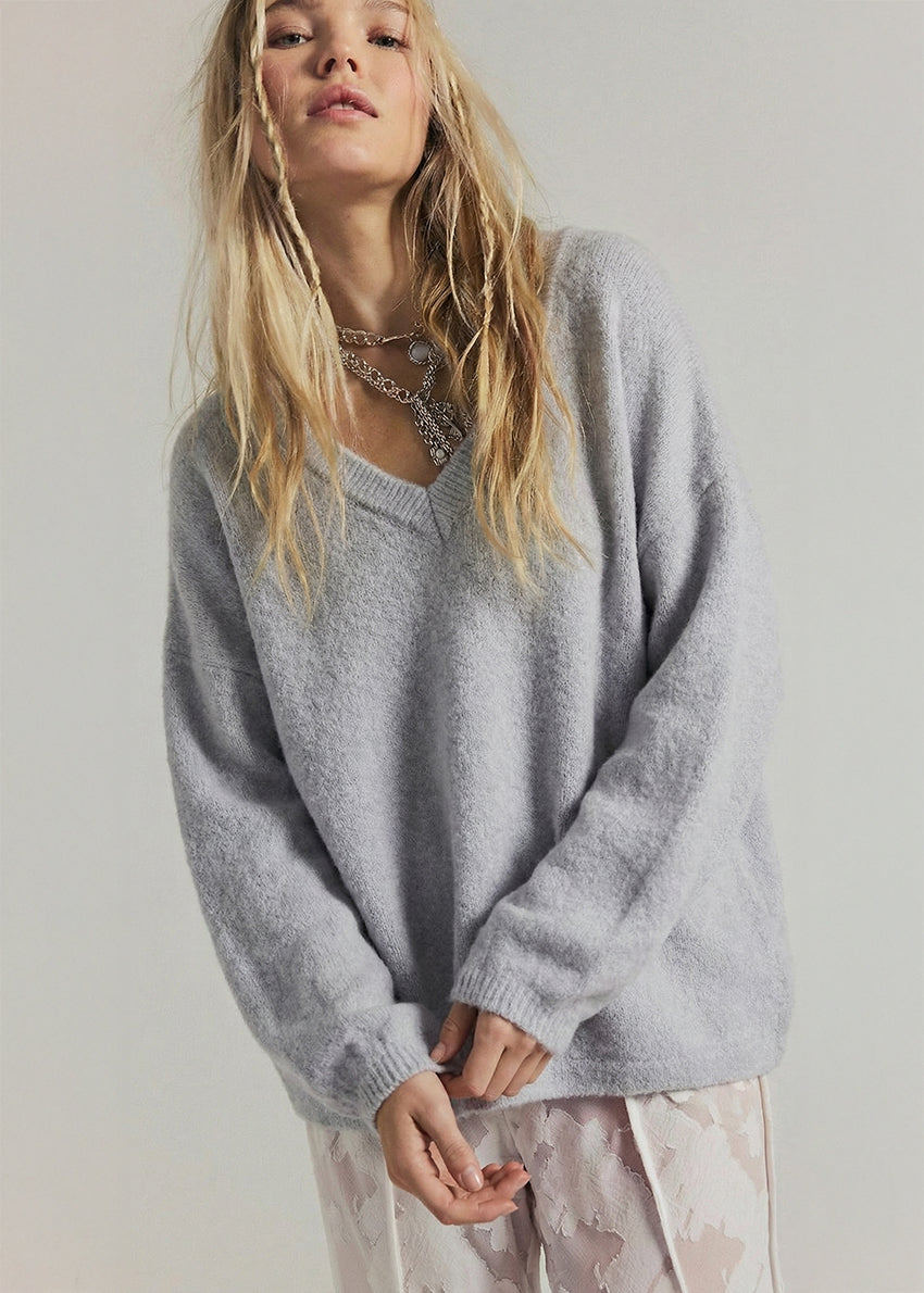 Woman wearing a gray oversized sweater against a plain background