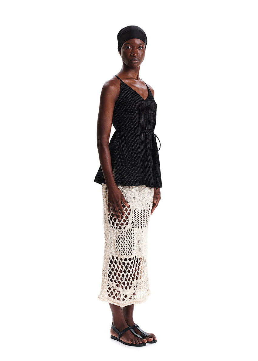 Woman wearing a black top and white crochet skirt on a white background