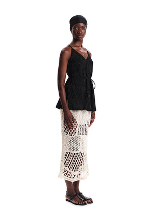 Woman wearing a black top and white crochet skirt on a white background