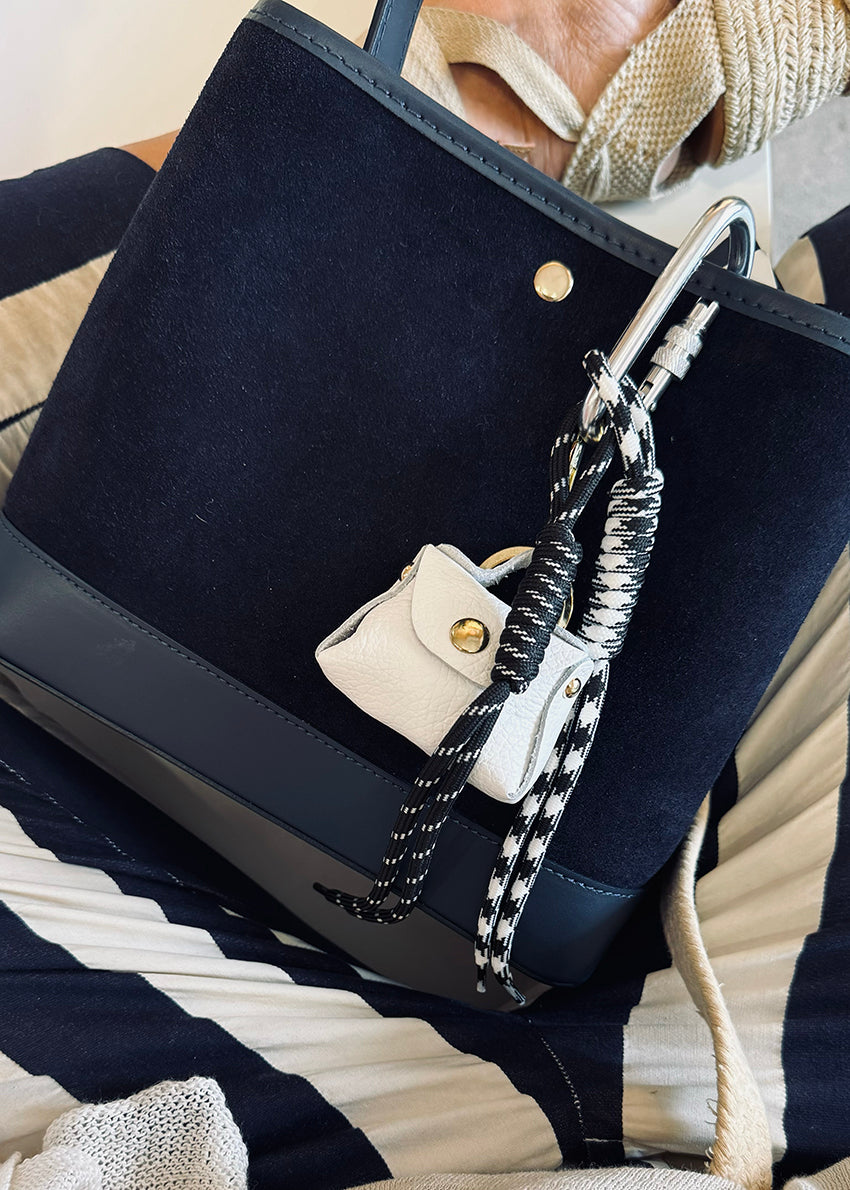 A multicolored braided rope keychain charm with heart shapes attached to a bag's zipper, displayed in a close-up image with a handbag in the background.