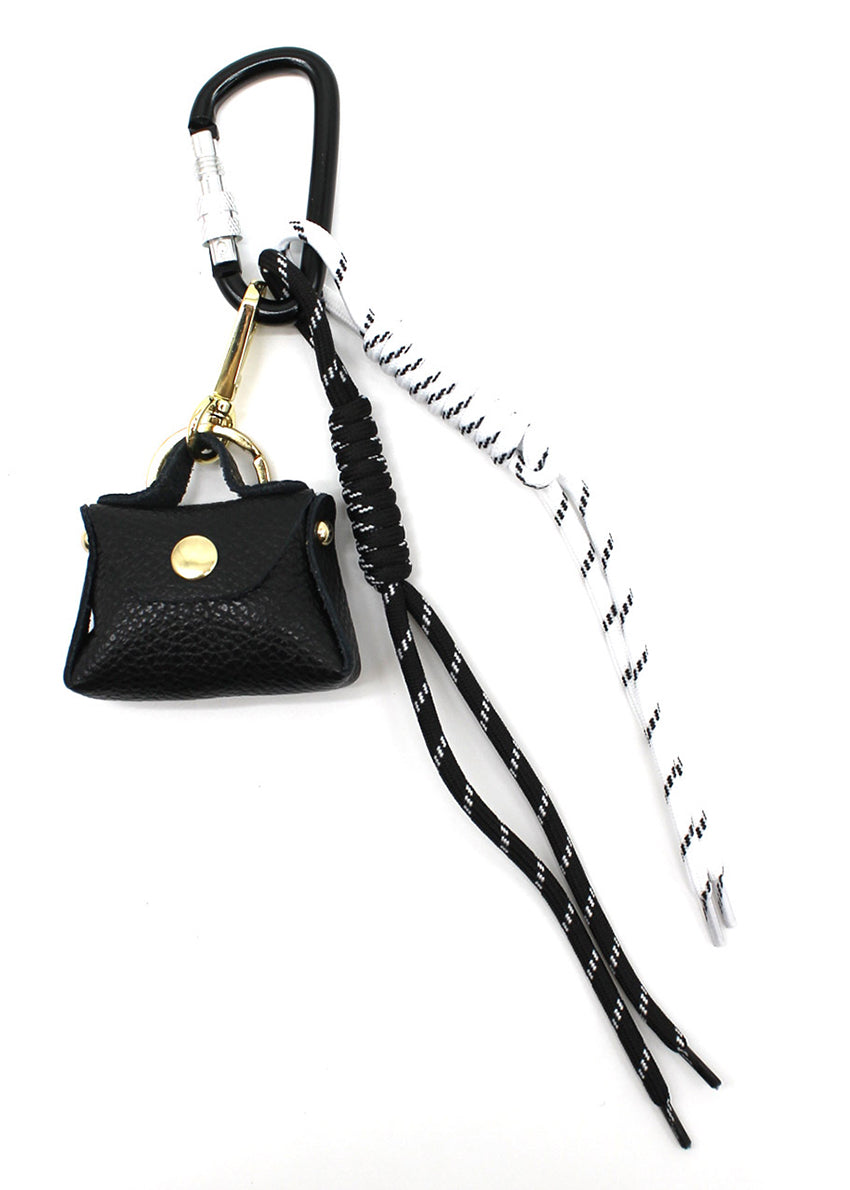 A multicolored braided rope keychain charm with heart shapes attached to a bag's zipper, displayed in a close-up image with a handbag in the background.