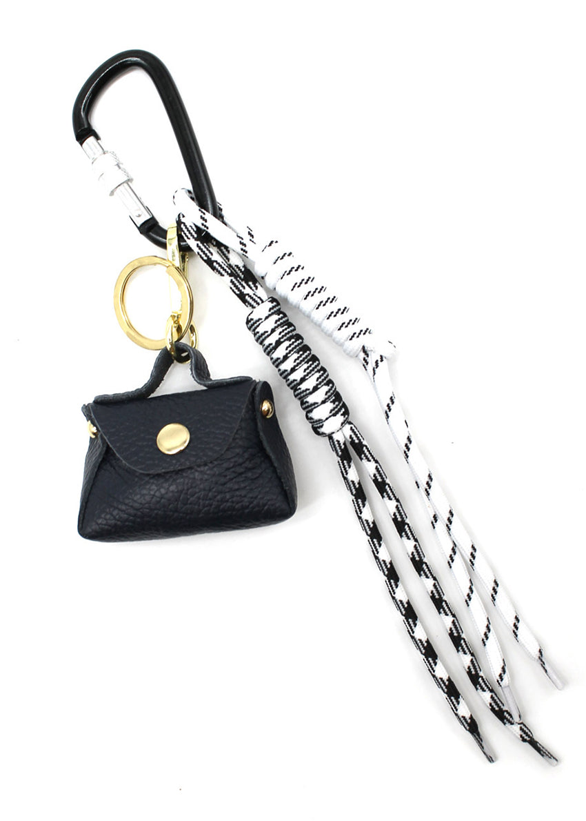 A multicolored braided rope keychain charm with heart shapes attached to a bag's zipper, displayed in a close-up image with a handbag in the background.