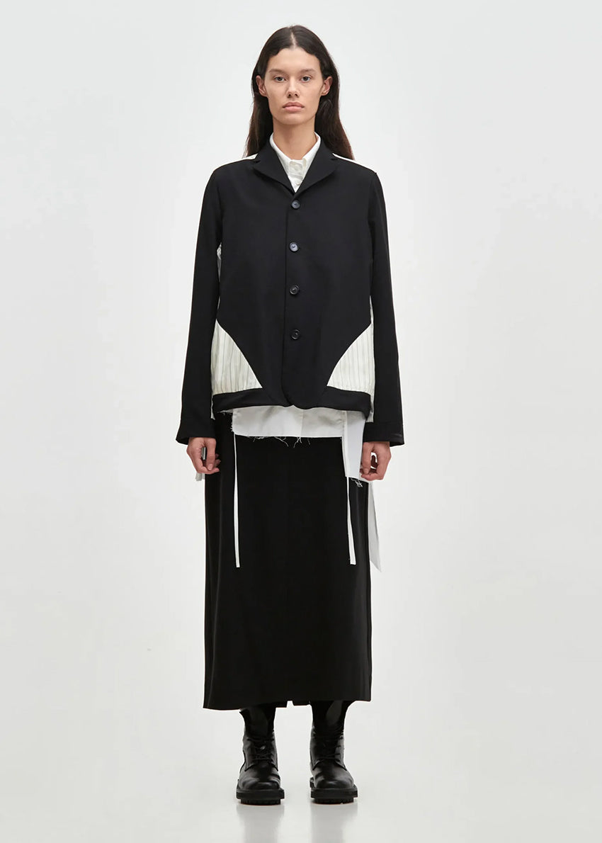 A model wearing a black and white geometric patterned short jacket with a lapel collar over a white shirt, paired with a black skirt and black boots.