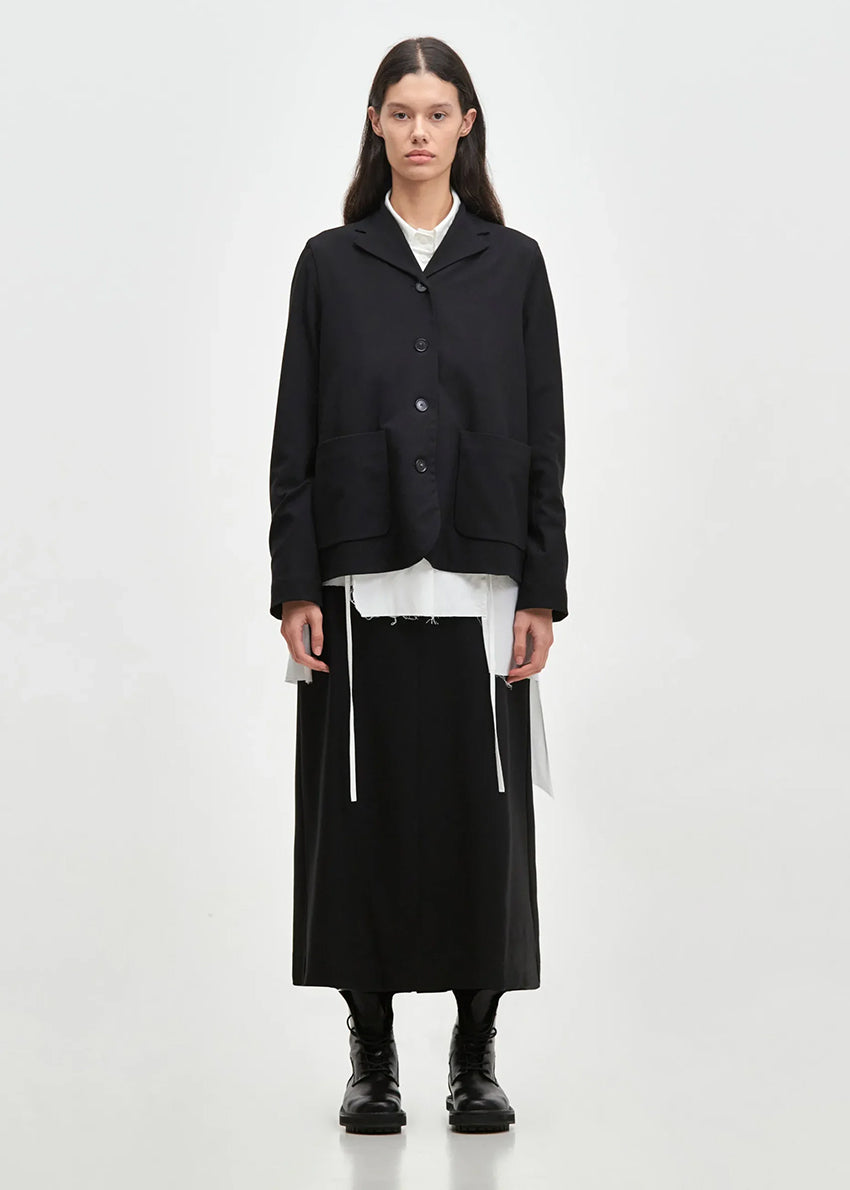 A model wearing a black and white geometric patterned short jacket with a lapel collar over a white shirt, paired with a black skirt and black boots.